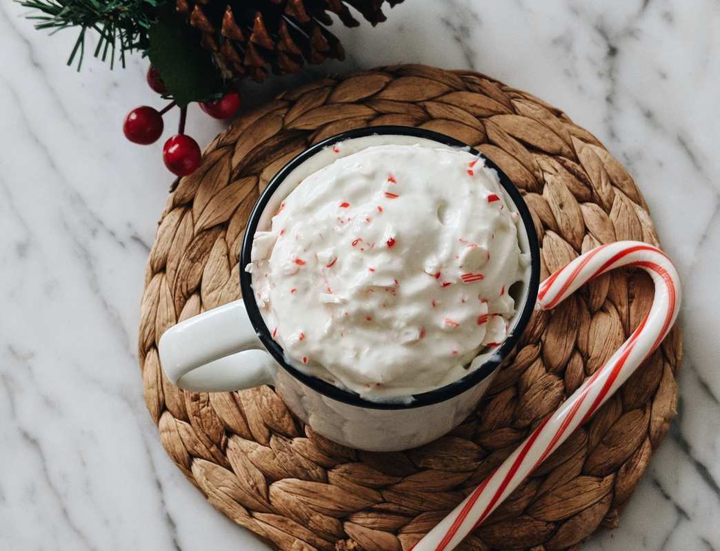 A cup of CBD hot cocoa rests on a wicker drink coaster, garnished with whip cream and an added candy cane and pine cone for decoration.