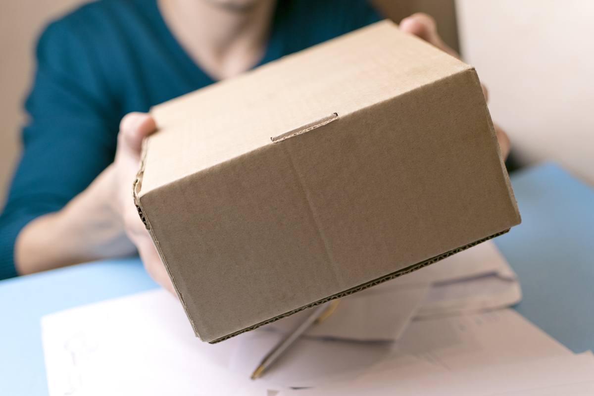 Point of view photo of a person mailing a cardboard box hands it off to a worker. Recent court rulings make it clear it's fully legal to send hemp by mail.
