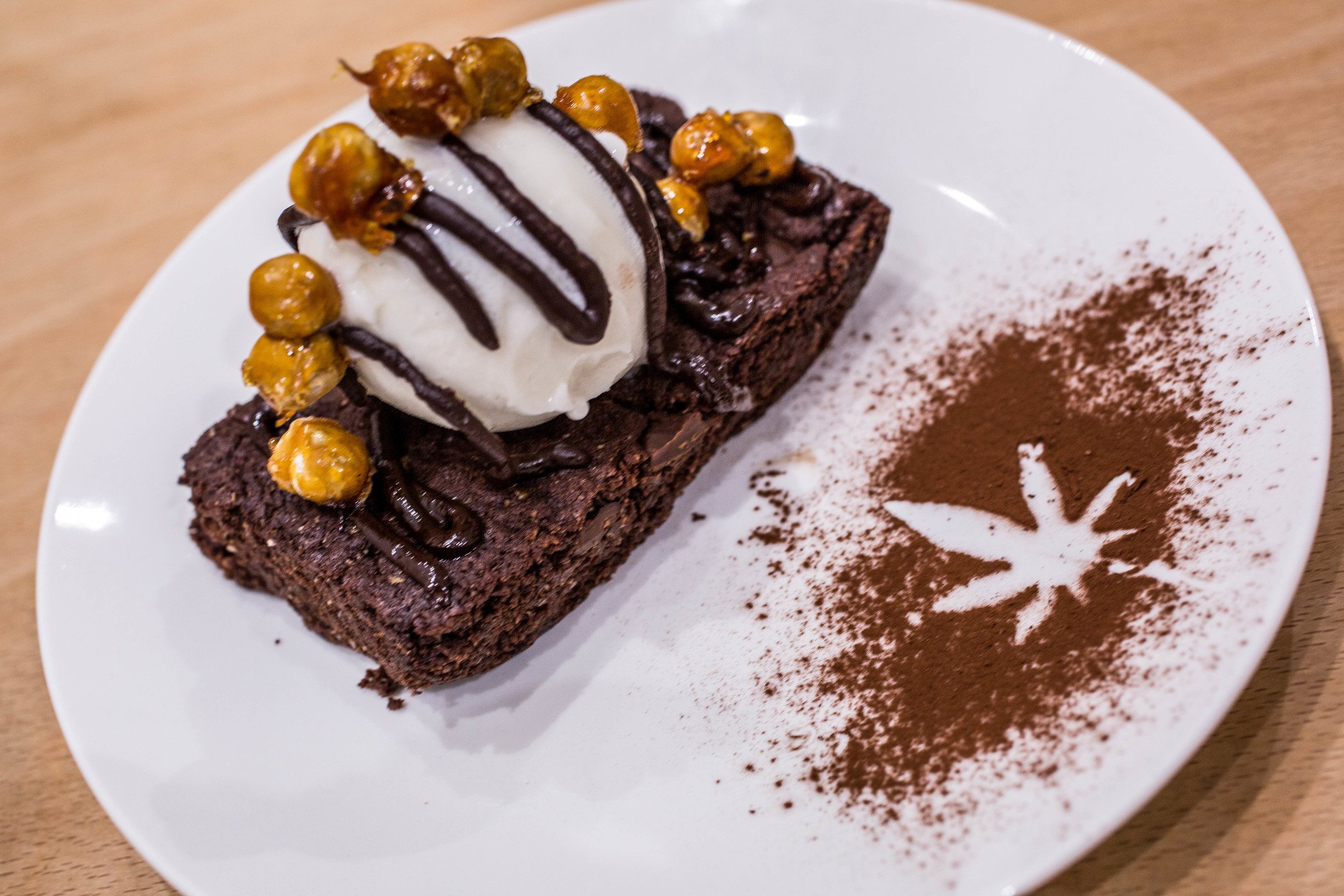 A decadent CBD-infused chocolate brownie a la mode, on a white plate decorated with a hemp leaf drawn in cocoa powder. The Canna Kitchen is the UK's first CBD restaurant, and it's making waves for their delicious vegetarian food.