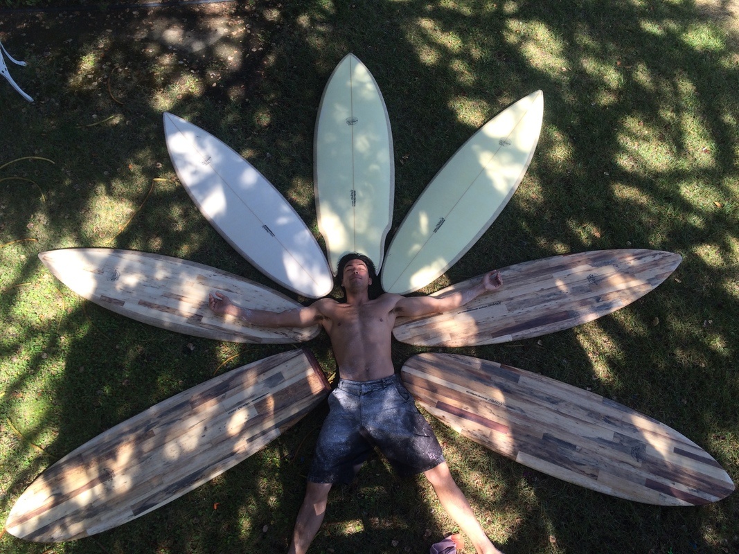 Photo: Chad Jackson laying on the ground surrounded by 7 of his hemp surfboards.