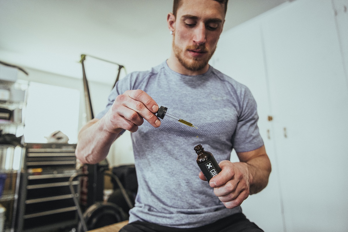 Athletes use CBD for recovery to reduce soreness after workouts, promote deeper sleep, and more. Photo: A man in gray workout clothes takes XWERKS CBD after exercise.