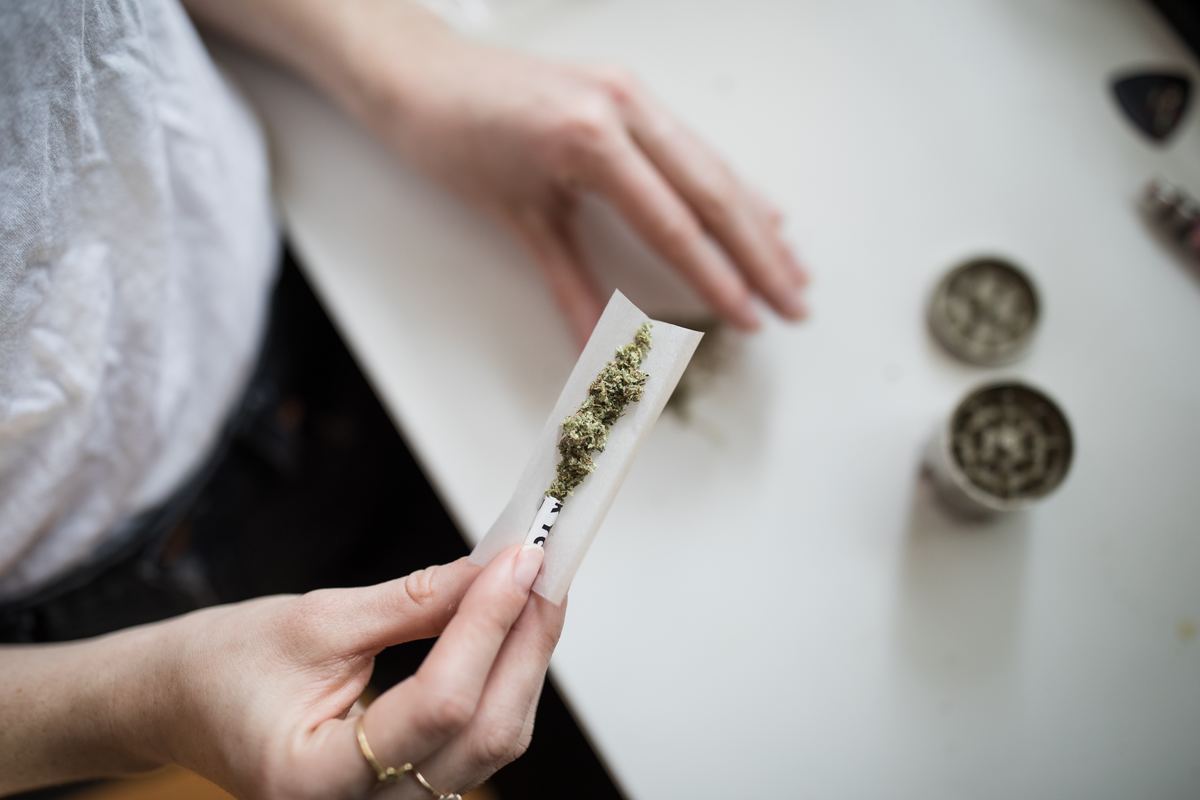 Whether you switch to cannabis flower, dab a concentrate, or eat an edible, there's numerous alternatives to vaping available. Photo: A person rolls a joint using a rolling paper and a filter, as well as broken up cannabis flower. A cannabis grinder is on a table nearby.