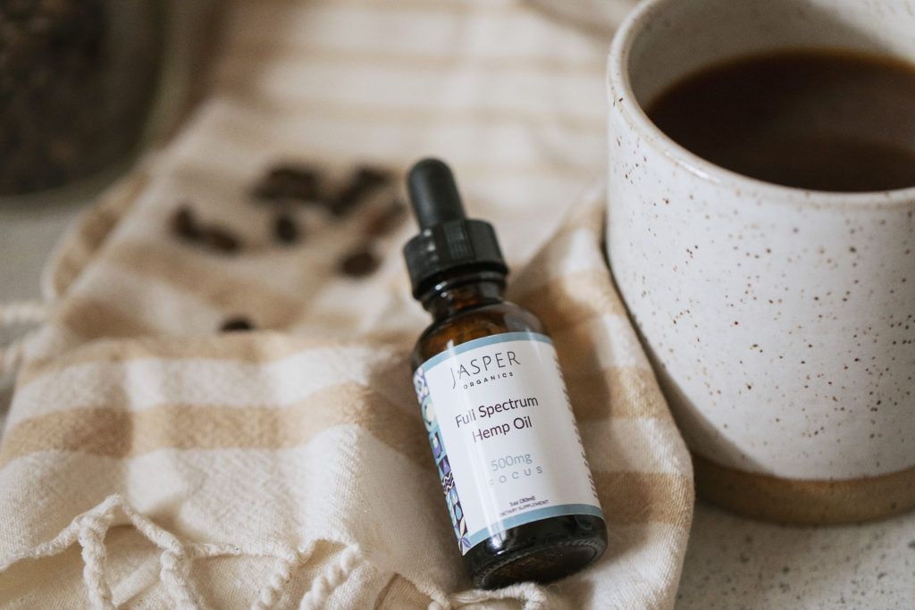 Jasper Organics Focus CBD is a great CBD for daytime use, or for new consumers of CBD. Photo: Jasper Organics Focus CBD posed with a mug of coffee and some coffee beans on a table cloth.