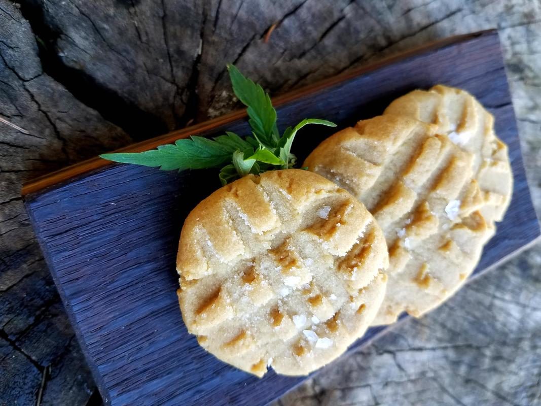 Peanut butter cookies garnished with a hemp leaf on a board on display.