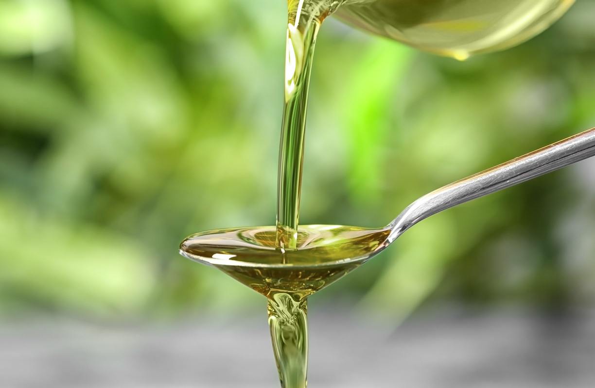 Photo: Hemp seed oil is poured onto an overflowing spoon from above. The background is blurry but green and organic.