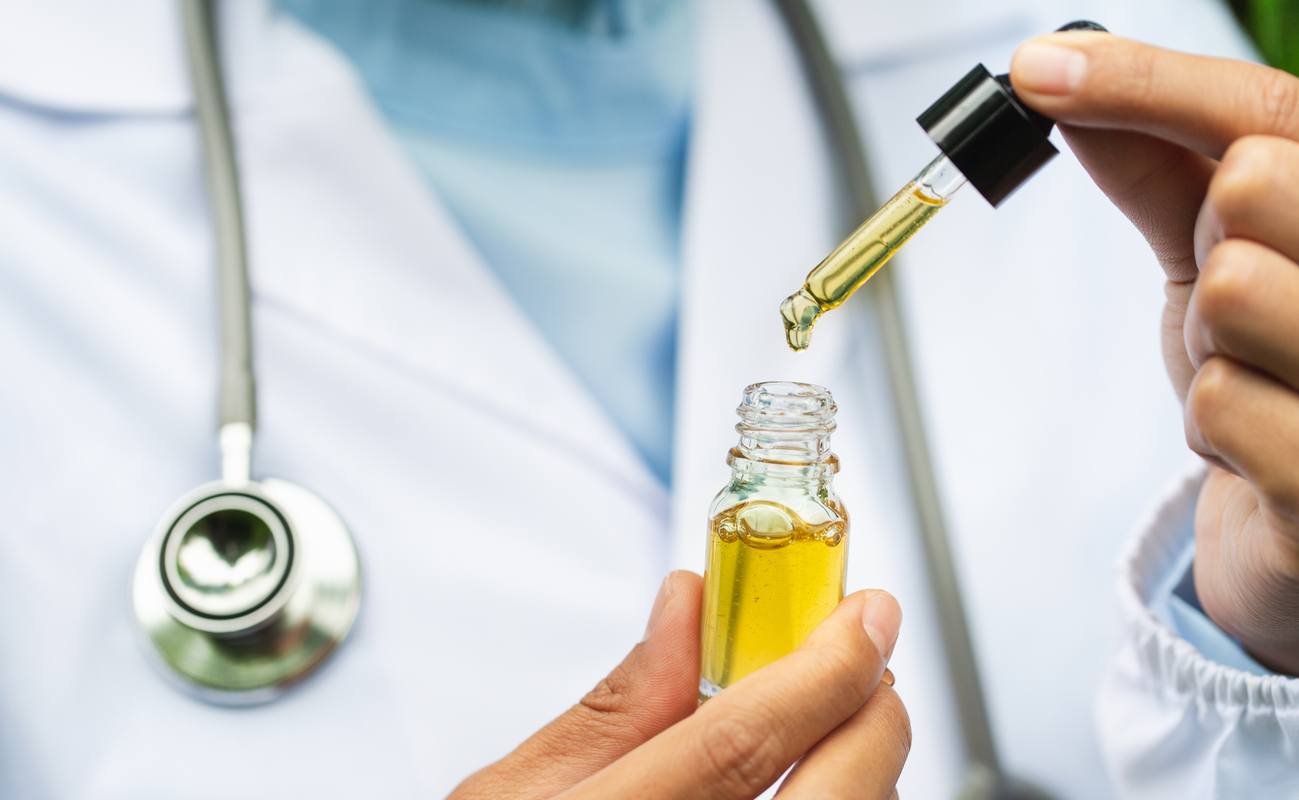 Matt and Kit answered CBD health questions on the Ministry of Hemp podcast, including questions about talking to doctors about CBD. Photo: A doctor wearing a lab coat and stethoscope, and holding a CBD bottle and dropper top.