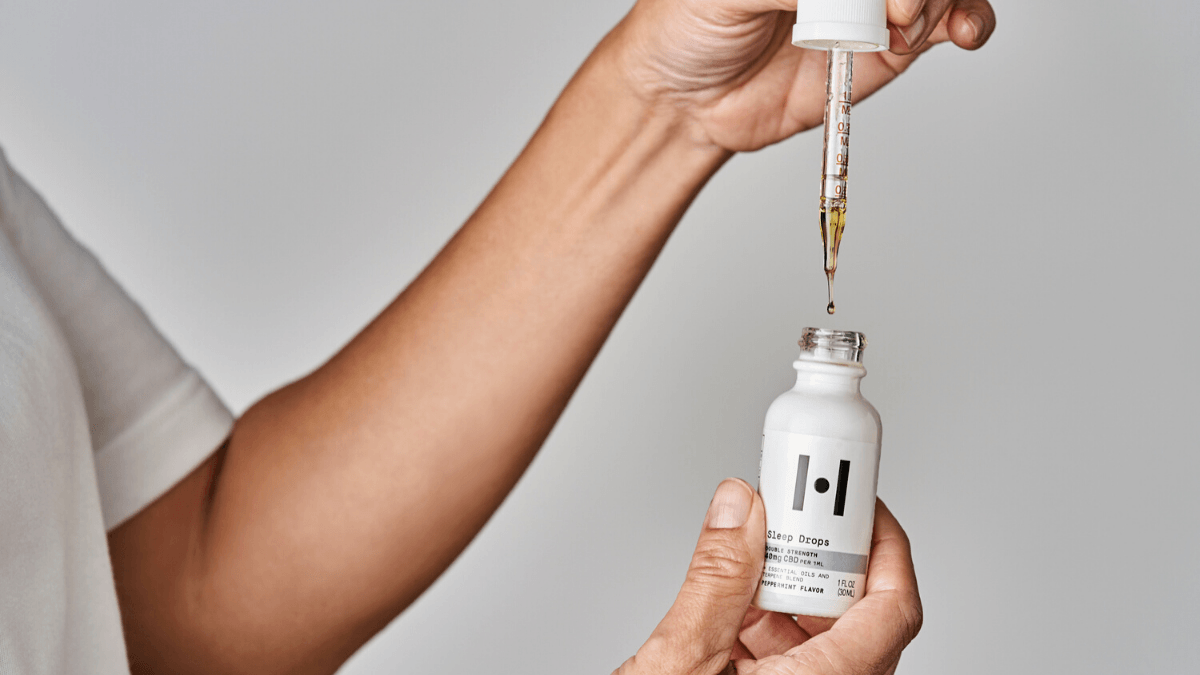 A person holds a bottle of Healist Naturals Sleep Drops in the double strength peppermint flavor, lettiing some drops fall from the dropper top back into the bottle.