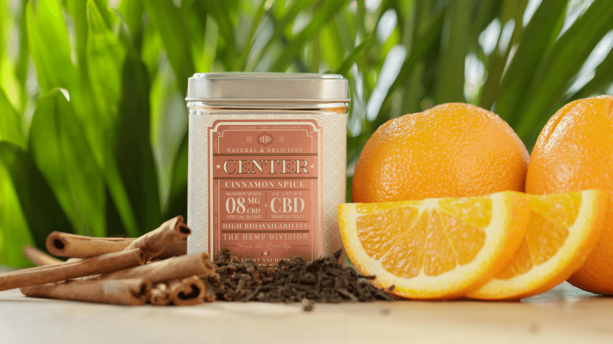 A tin of Cinnamon Spice CBD tea from Harney & Son's The Hemp Division, posed with oranges and cinnamon sticks.