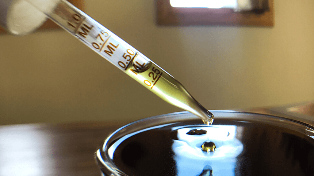 A dropper of broad spectrum CBD oil held over a drinking glass of water, with droplets falling into a beverage.