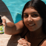 A smiling woman with dark hair, in a swimming pool, holds up a bottle of Sir Hemp Co CBD.