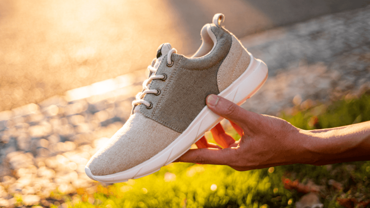 A hand holds up a single hemp sneaker in a natural gray with a white bioplastic sole. Hemp shoes could be an important part of a more sustainable future.