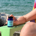 A seated woman at the beach in a sun hat, face just out of frame, holds a bottle of Hemp Mellow.