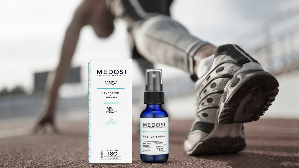A Medosi Energy Spray box and bottle resting on an outdoor track behind a runner crouched in the ready position.